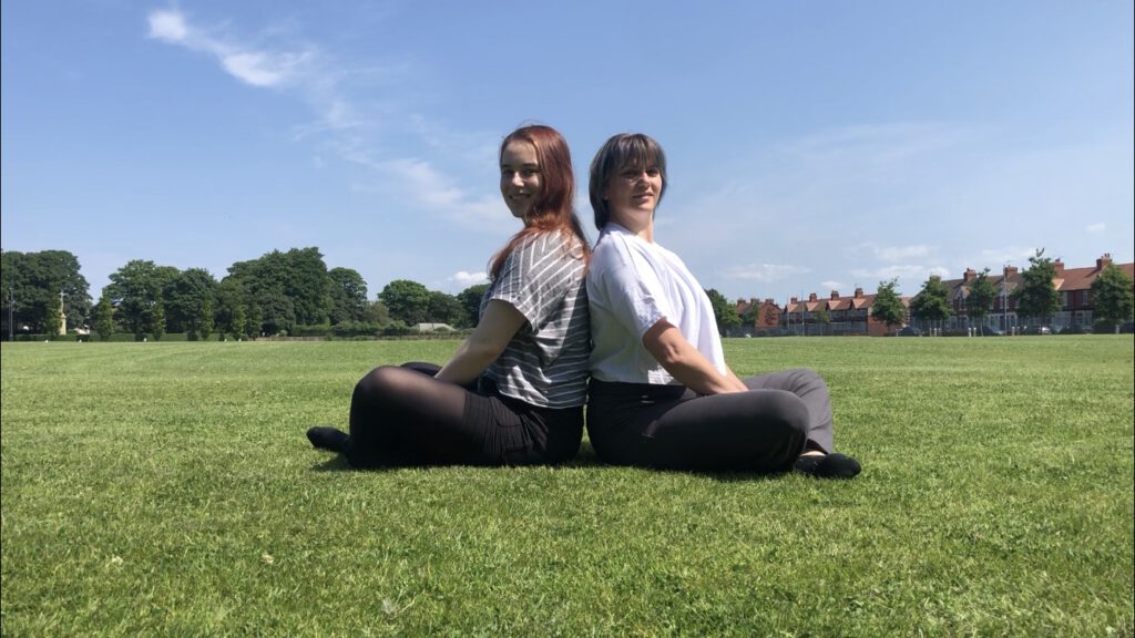 Image of alissa and corinne both female sitting on grass looking into the camera smiling.