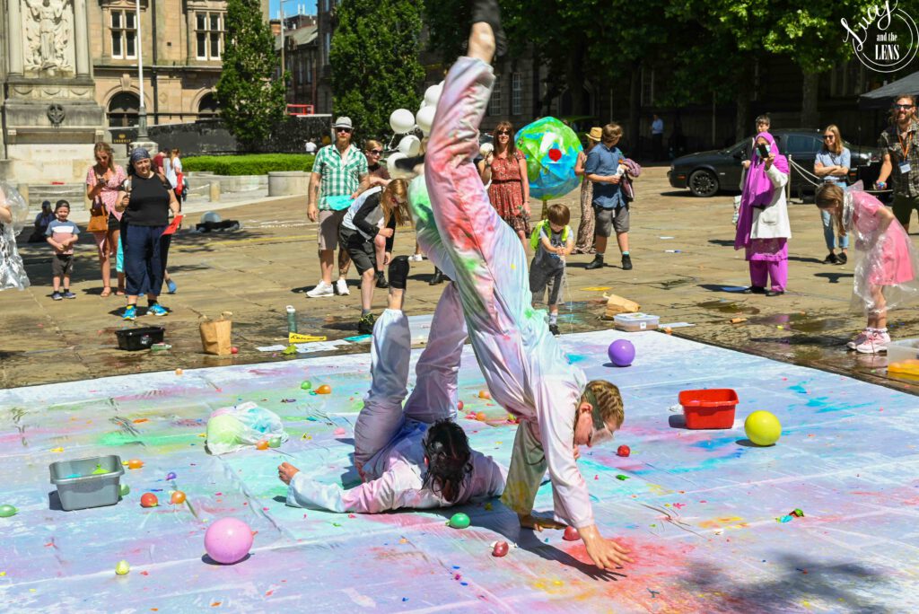 Two performers in the space covered in colourful paint