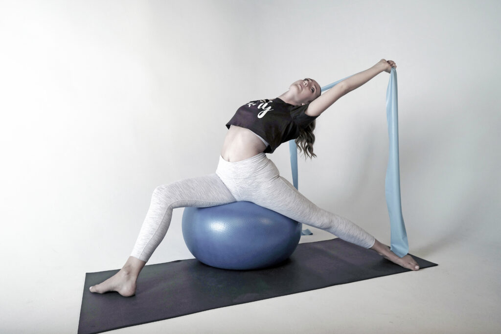 Image of a female dancer on a fit ball stretching backwords.